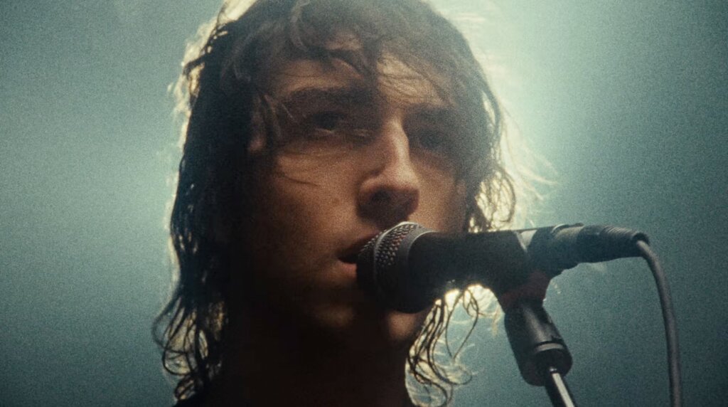 Cameron Winter sings into a microphone, a light behind his head halo-ing his appearance.