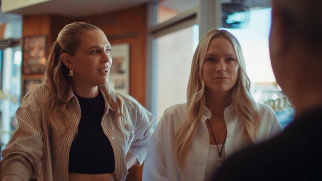 Erin Foster and Sara Foster talk to a man in a shop. The man's back is turned and we see only his shoulder and a small portion of his face.