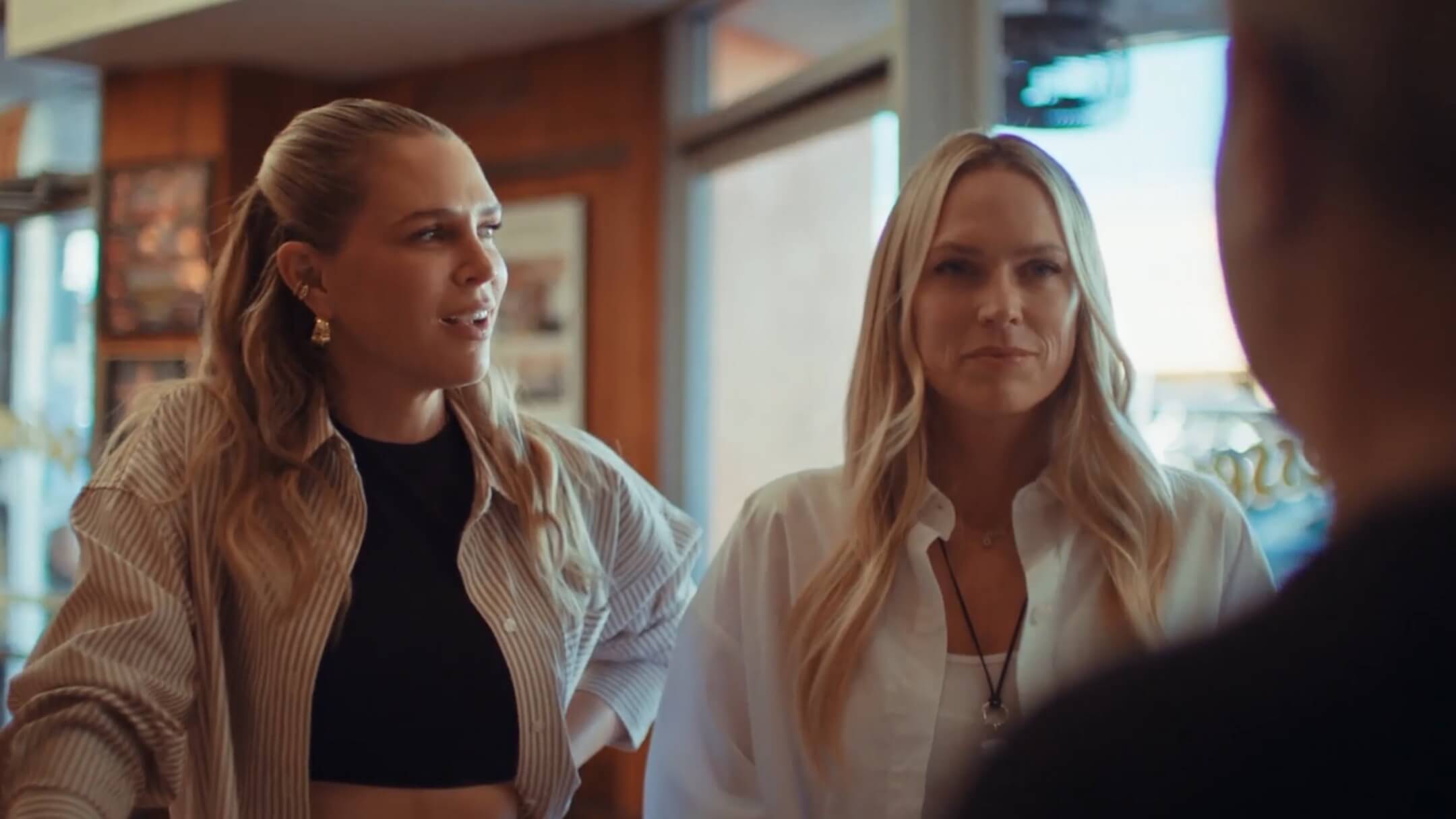 Erin Foster and Sara Foster talk to a man in a shop. The man's back is turned and we see only his shoulder and a small portion of his face.